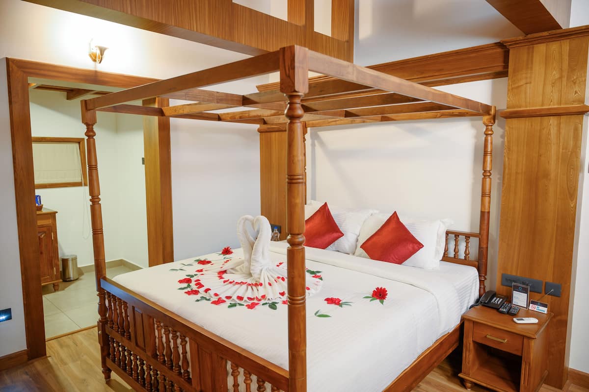 Una cama con dosel con cubrecama blanco y almohadas rojas, una mesita de noche con un teléfono y una tarjeta de identificación, y un tocador de madera.