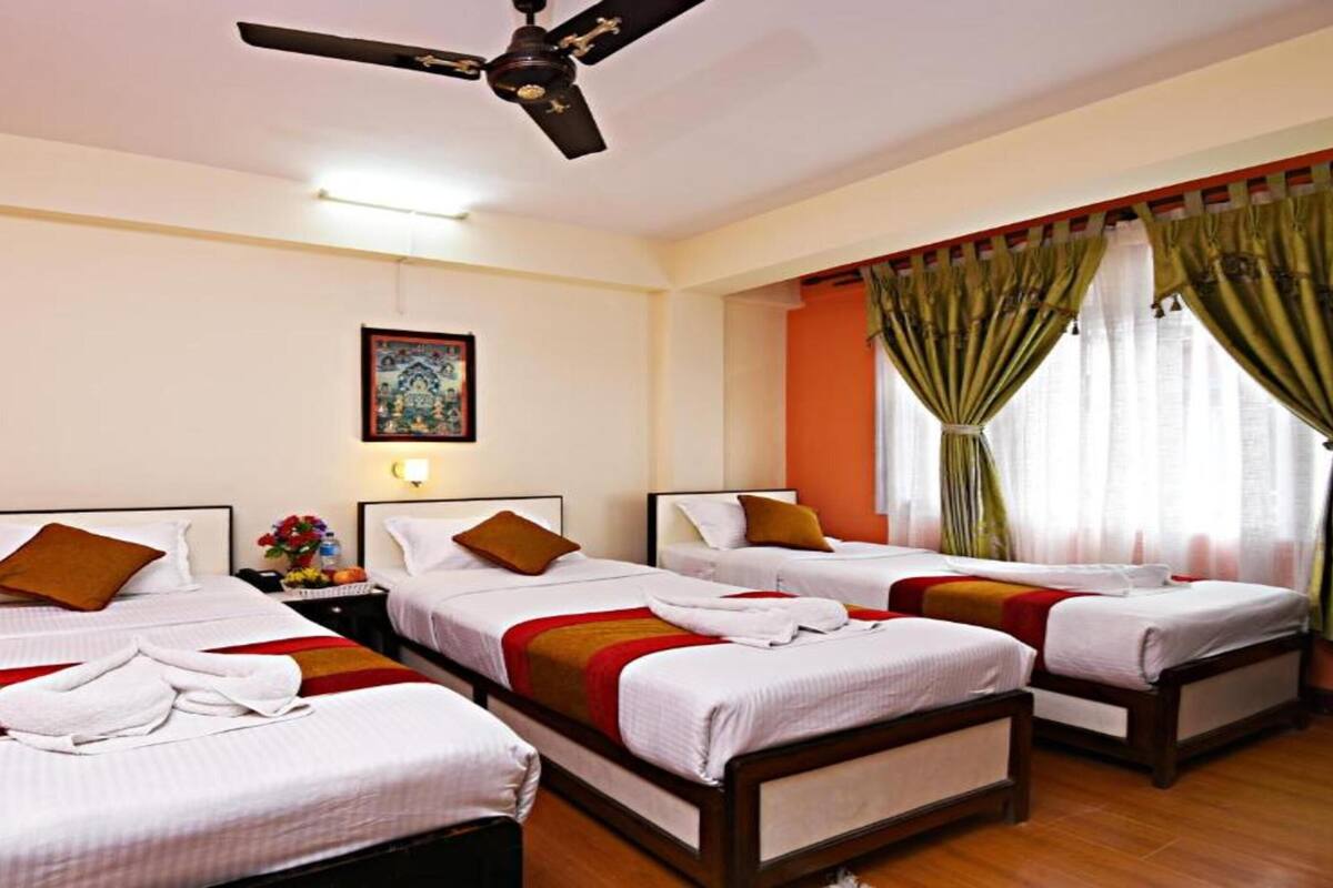 A hotel room with three single beds, a ceiling fan, a framed picture on the wall, and a window with curtains.