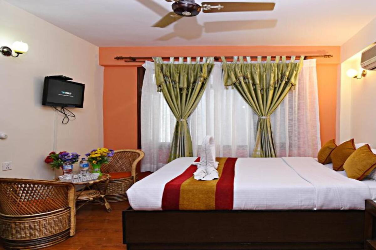 A hotel room with a bed, a chair, a table with flowers, and a TV.