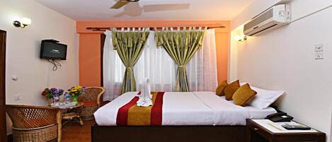 A hotel room with a bed, a chair, a table with flowers, and a TV.