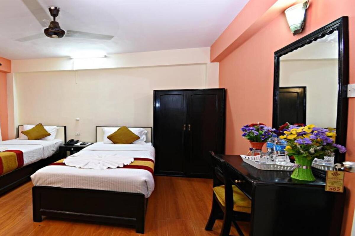 A hotel room with two single beds, a desk with a mirror, a wardrobe, and a ceiling fan.