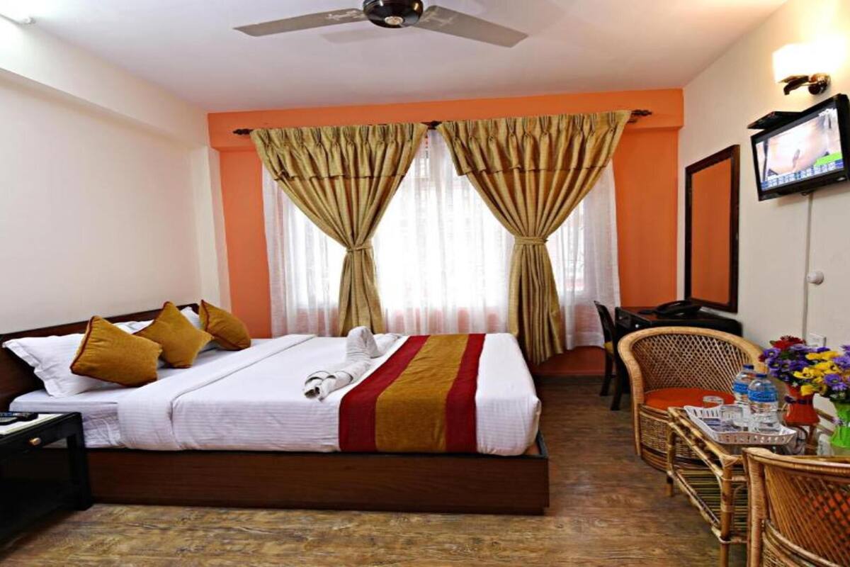 A hotel room with a bed, a desk with a chair, a television, and a small table with flowers.