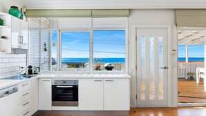A modern kitchen with a view of the ocean, white cabinetry, and a built-in oven. - Charming Beach Cottage - 39 Kianga Parade (Kianga)