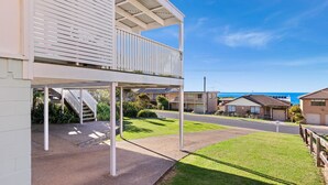 A two-story residential building with a balcony, a covered outdoor area, and a view of the ocean. - Charming Beach Cottage - 39 Kianga Parade (Kianga)
