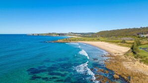 A coastal landscape with a sandy beach, clear blue waters, and rocky outcrops. - Charming Beach Cottage - 39 Kianga Parade (Kianga)