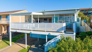 A two-story house with a balcony, a covered patio, and a small garden area. - Charming Beach Cottage - 39 Kianga Parade (Kianga)