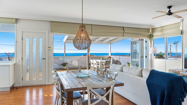 A spacious room with a wooden dining table, white chairs, and a sofa with a blue throw. - Charming Beach Cottage - 39 Kianga Parade (Kianga)