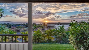 A balcony with a view of a sunset over a residential area, including houses and greenery. - Wailea Ekolu – Oceanview in the Heart of Wailea (Kihei)
