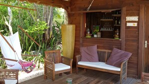 Een houten chalet met een houten tafel, twee stoelen, een bank en een barruimte met flessen op de planken.