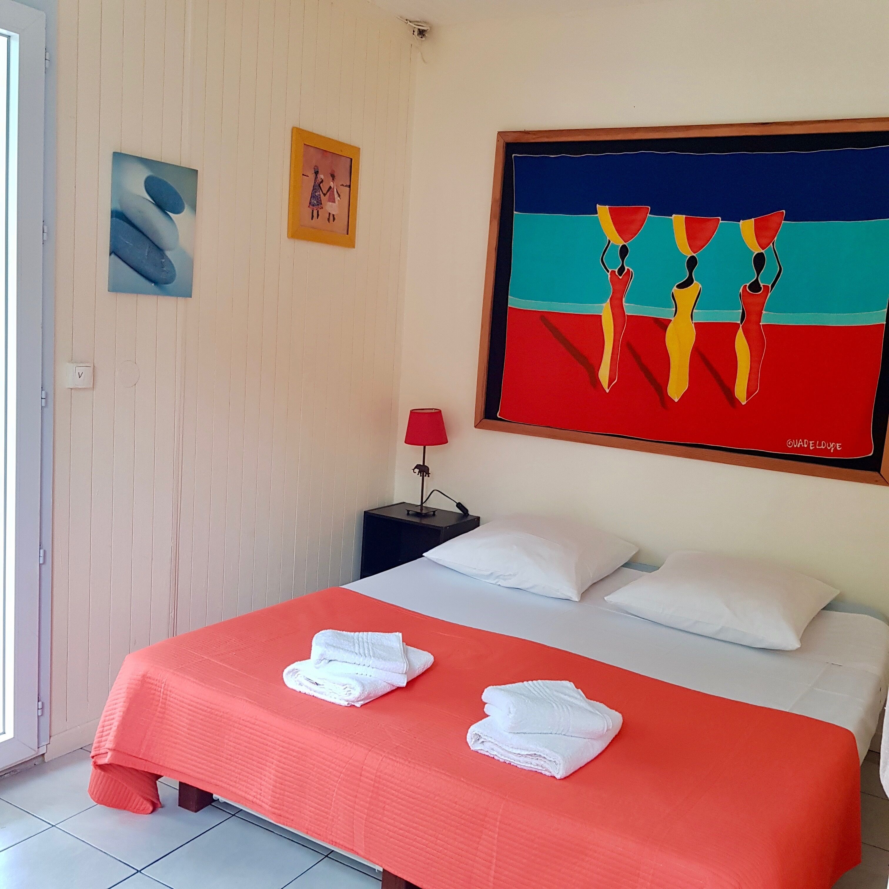 Een hotelkamer met een bed, twee kussens, een nachtkastje met een lamp en twee schilderijen aan de muur.