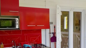 Een kleine keuken met rode kastjes, een magnetron, een koelkast, een spoelbak en een fornuis.