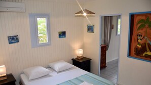 Een slaapkamer met een bed, een nachtkastje met een lamp, een raam en een deur naar een andere kamer.
