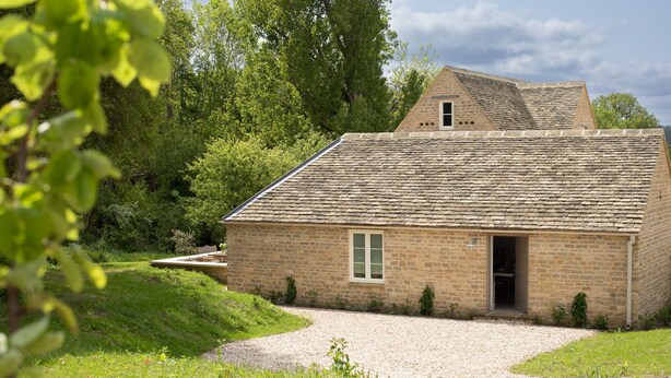 Un bâtiment en pierre avec un toit en pente, une petite fenêtre et une allée gravillonnée.