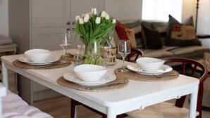 Une table à manger dressée avec de l’assiette, des bols et des couverts blancs, agrémentée d’un vase de tulipes blanches et de verres à vin.