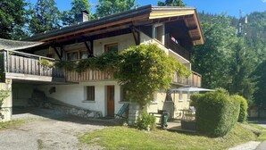 Un chalet de dos pisos con balcón de madera, base de piedra y un pequeño jardín.