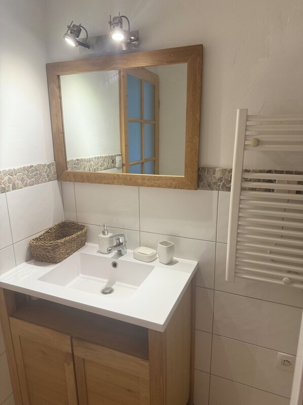 A bathroom with a white sink, a wooden cabinet, a mirror with a wooden frame, a towel rack, and a window with blue shutters.