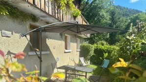 Un patio con mesa y sillas, una terraza de madera y vistas a una ladera boscosa.