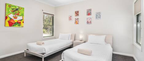 A hotel room with two single beds, a window with a view of greenery, and several wall art pieces.