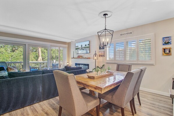 A spacious living area with a large window overlooking a deck, a dining table with chairs, and a fireplace.