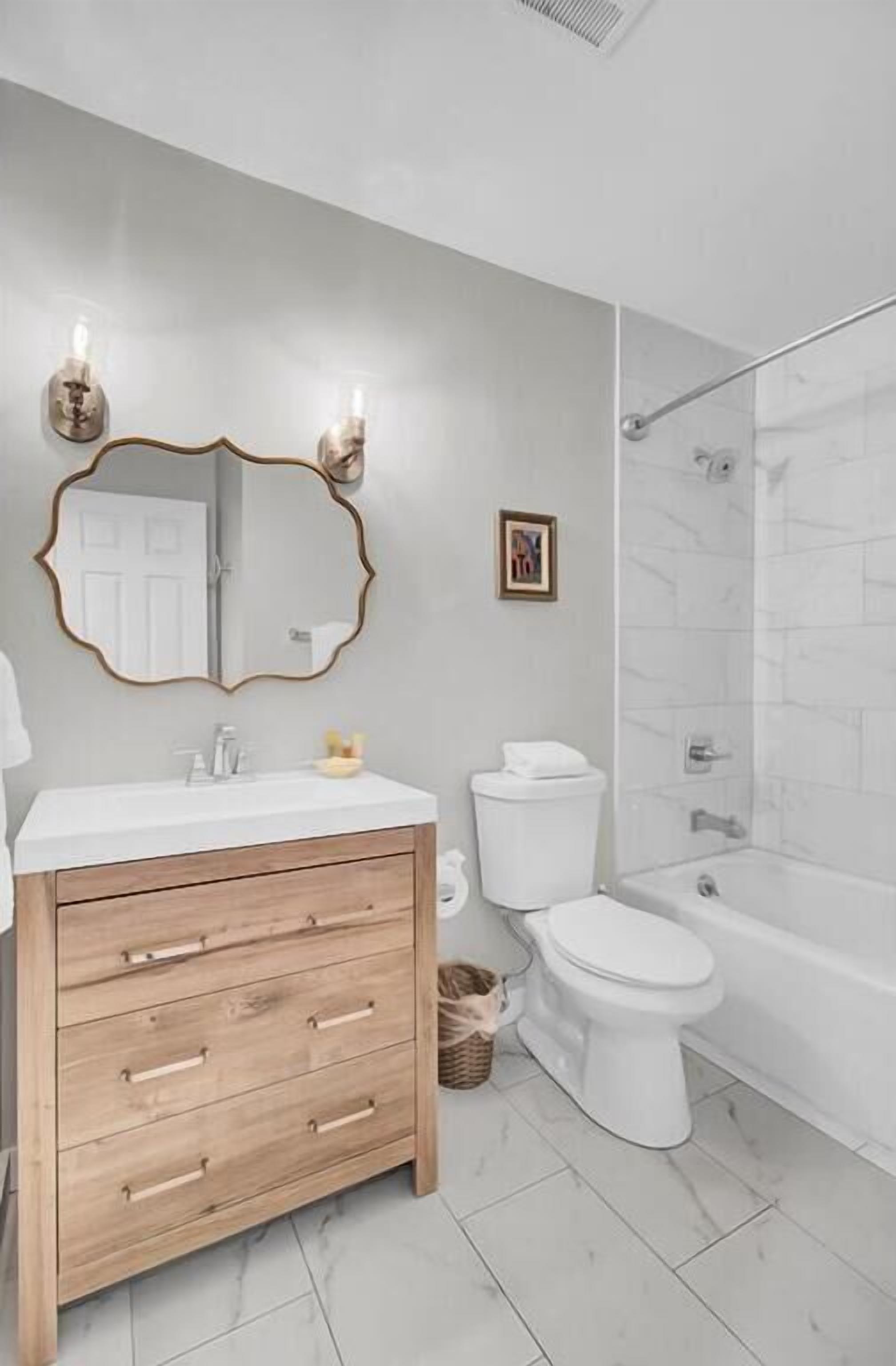 Un baño con tocador de madera, inodoro blanco, cabina de ducha de vidrio y un cuadro en la pared.