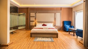 Una habitación de hotel moderna con una cama grande, un box de ducha de vidrio, un sillón azul y una pequeña mesa.