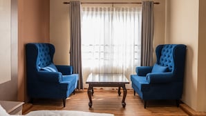 Una habitación con dos sillones azules, una mesa con cubierta de vidrio y una ventana con cortinas.