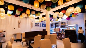 Un área de comedor con una mesa y sillas de madera, una pared blanca decorada con un atrapasueños, y una zona de bar al fondo.