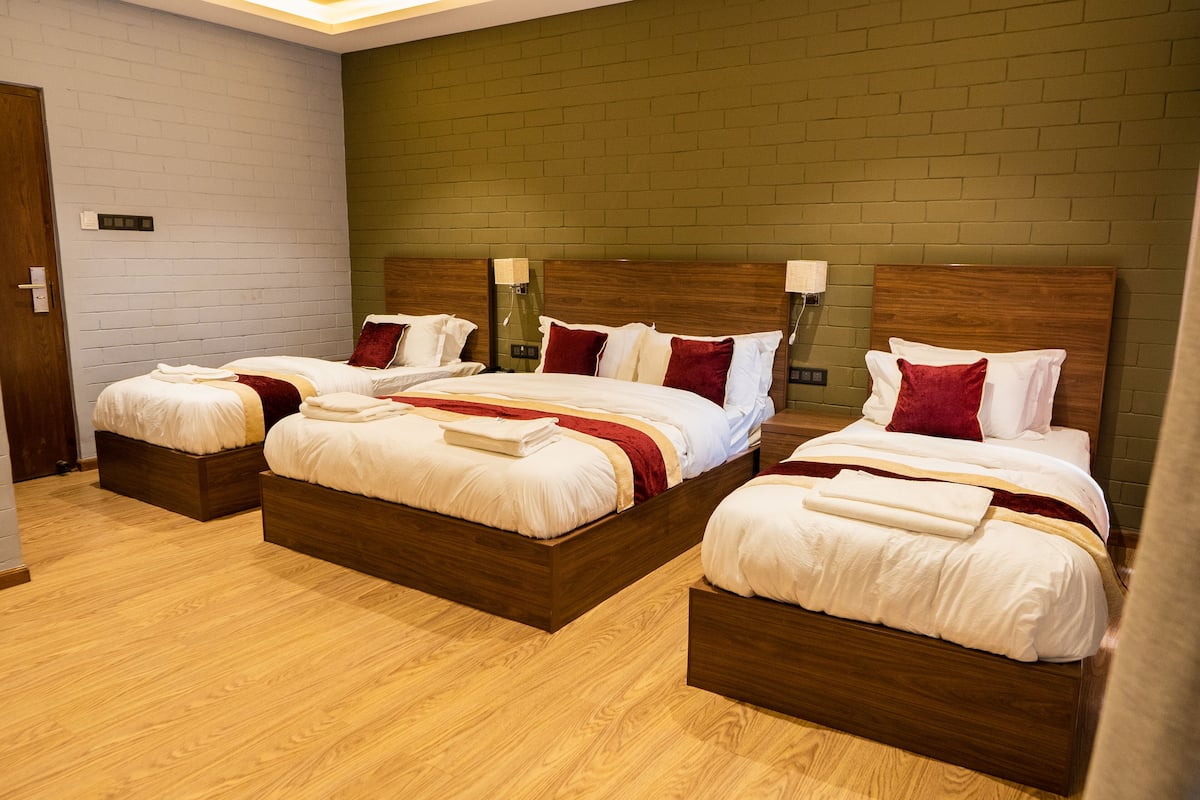 Habitación de hotel con tres camas de madera, cada una con ropa blanca y detalles rojos.