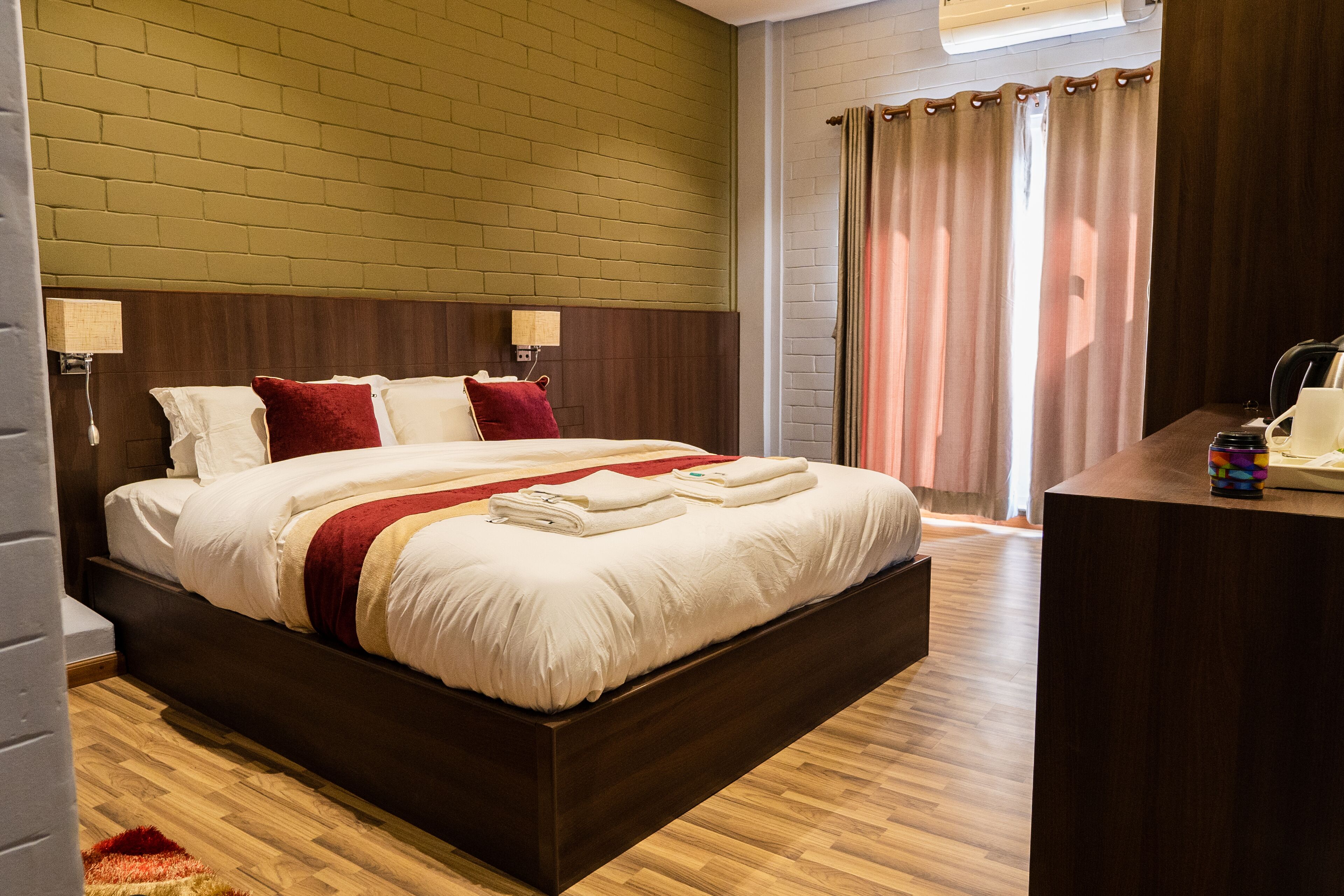 A modern hotel room with a large bed, wooden headboard, and a desk with a lamp.