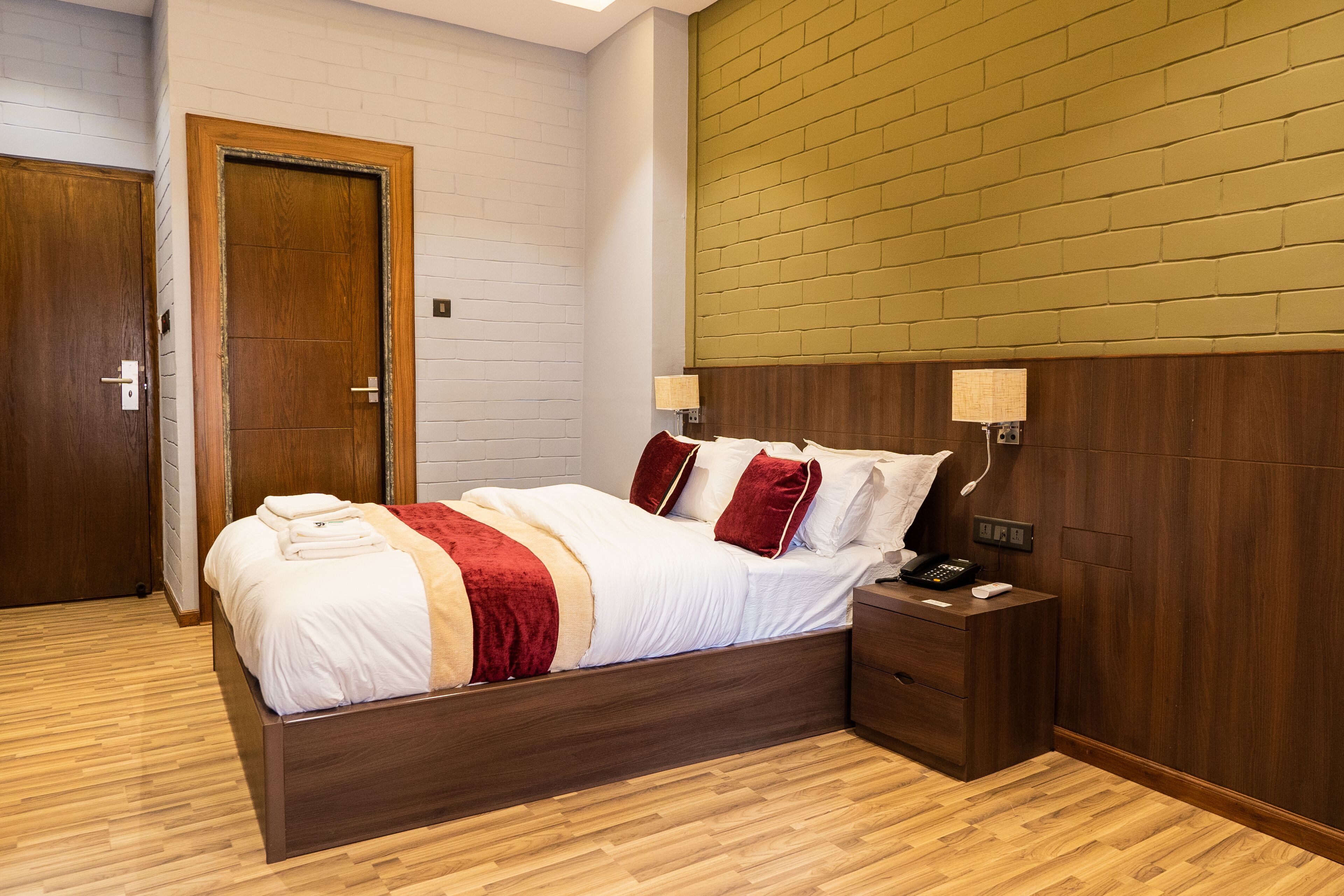A neatly arranged bedroom with a wooden bed, a nightstand, and a wall-mounted lamp.