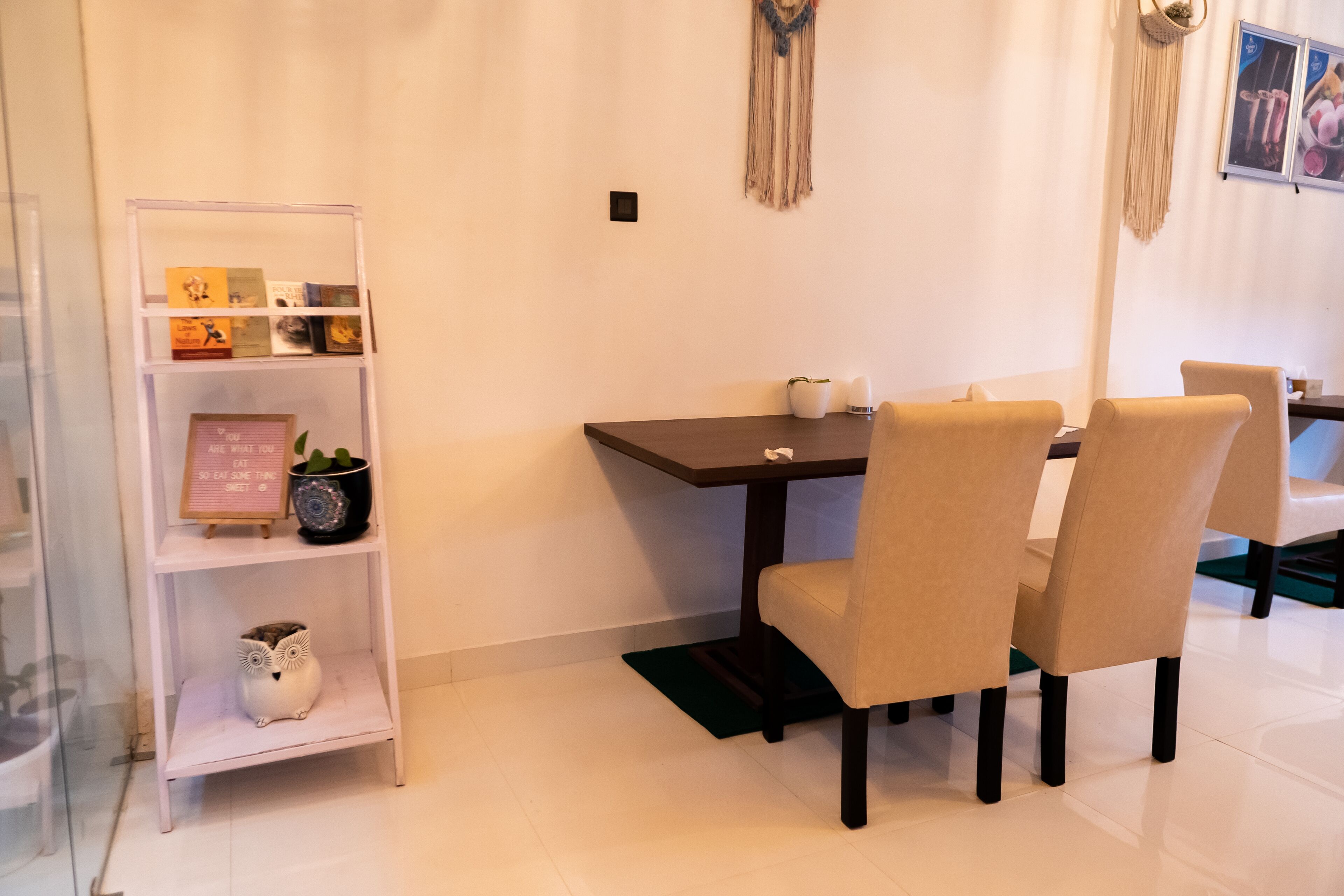 A dining area with a table, chairs, a bookshelf, and a decorative macrame wall hanging.
