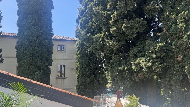Una terrazza con un tavolo apparecchiato per un pasto, completa di una bottiglia di vino, bicchieri e ciotole di snack.