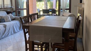 Zona pranzo con tavolo e sedie in legno, lampadario e ampie finestre con tende.