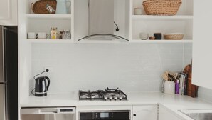 Een keuken met witte kastjes, een gasfornuis, een waterkoker en diverse keukengerei.