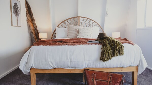 A neatly made bed with a white duvet, a brown throw blanket, and a green fringe throw. There is a wooden headboard, two bedside lamps, and a brown leather bag on the bed. - Reardon Retreat - A stones throw to the beach (Port Fairy)