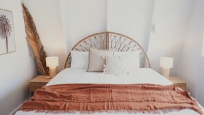 Een bed met een geweven hoofdbord, twee bedlampjes, een grote decoratie van veren, en een lijst met een foto aan de muur.