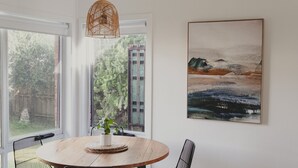 Een eetruimte met een ronde houten tafel, een hangende rieten lamp en een lijstwerk schilderij van een landschap aan de muur.