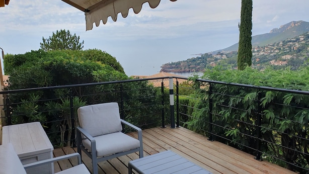 Une terrasse en bois avec une chaise et une table, d’où l’on a vue sur une ville côtière, avec des montagnes en arrière-plan.