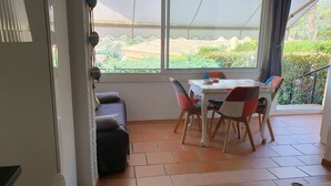 Un coin repas comprenant une table et des chaises, un canapé et une vue sur un jardin grâce à de grandes fenêtres.