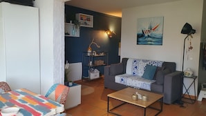 Un salon comprenant un canapé, une table basse et un tapis à motifs. On y trouve une étagère avec des objets décoratifs et un tableau accroché au mur.