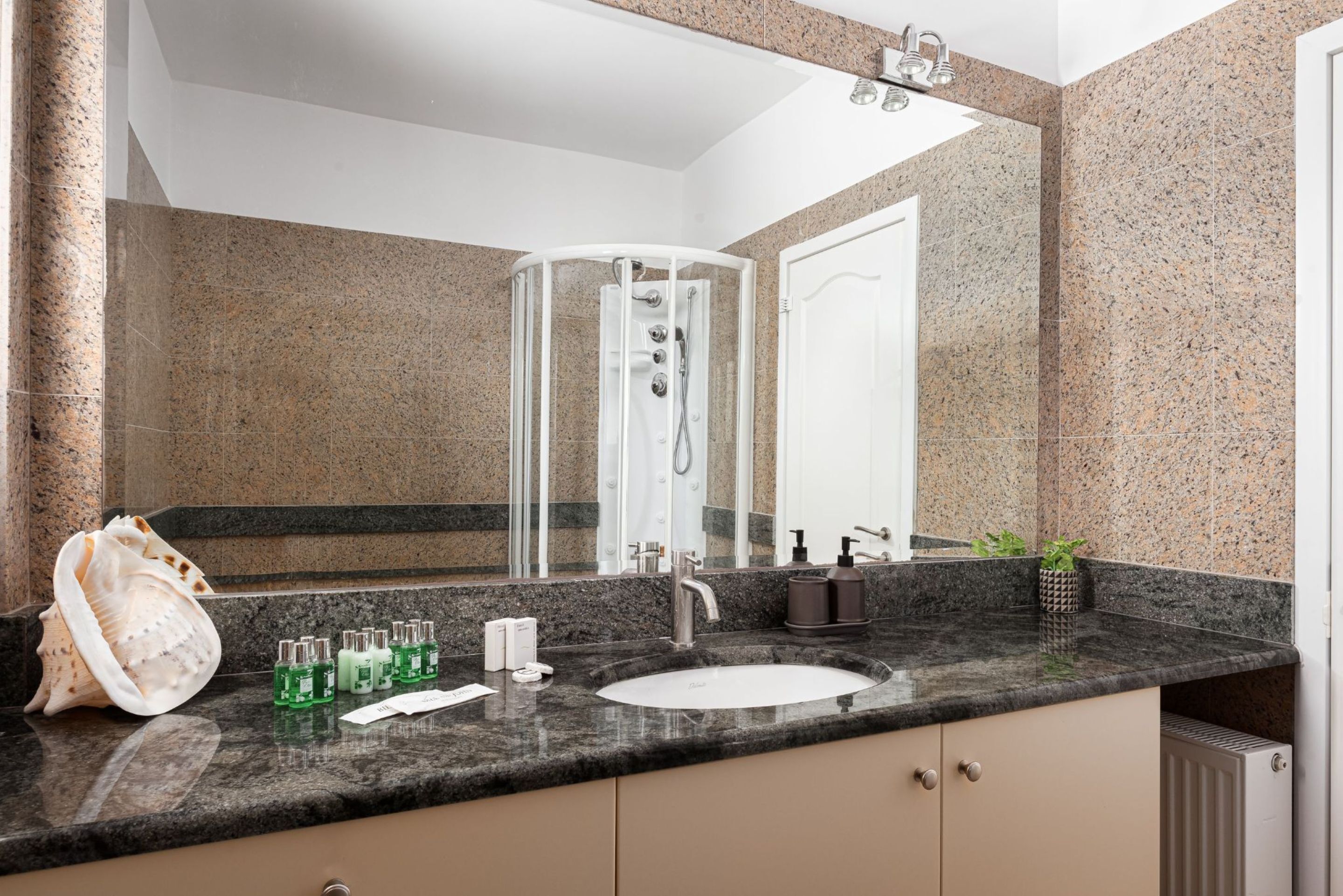A modern bathroom with a granite countertop, a white sink, a glass-enclosed shower, and a large mirror.