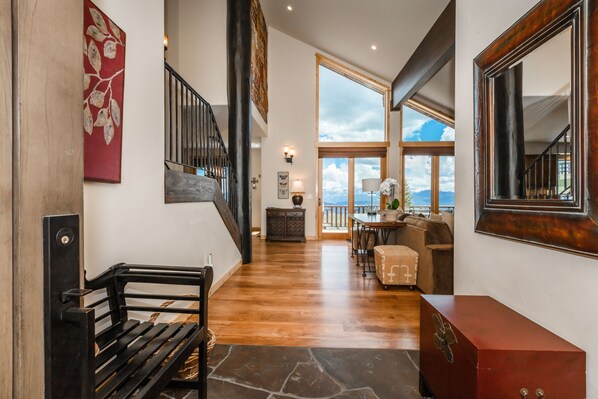 A spacious hallway with a wooden bench, a stone floor, and a view to a balcony with a scenic landscape.