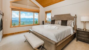 Une chambre avec un grand lit, un banc, une table de chevet et une vue sur les montagnes grâce à de grandes fenêtres.