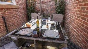 Mesa de jantar posta para dois, com garrafa de vinho, copos, pratos e talheres.