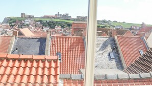 Vista de uma cidade com telhados vermelhos e um castelo histórico em uma colina ao fundo.