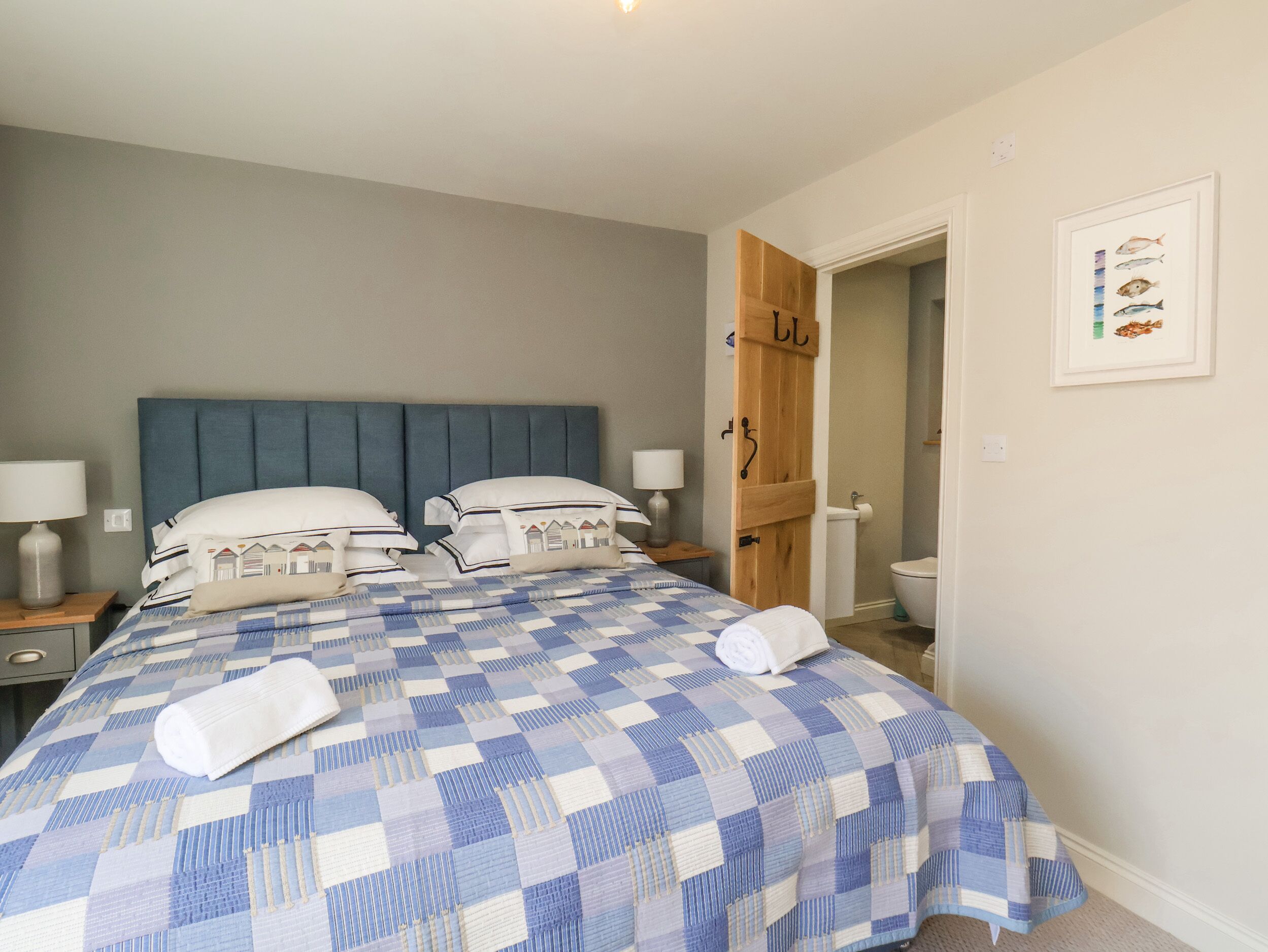 Een slaapkamer met een groot bed, twee nachtkastjes met lampen, een houten garderobe en een illustratie van een vis in een lijst aan de muur.
