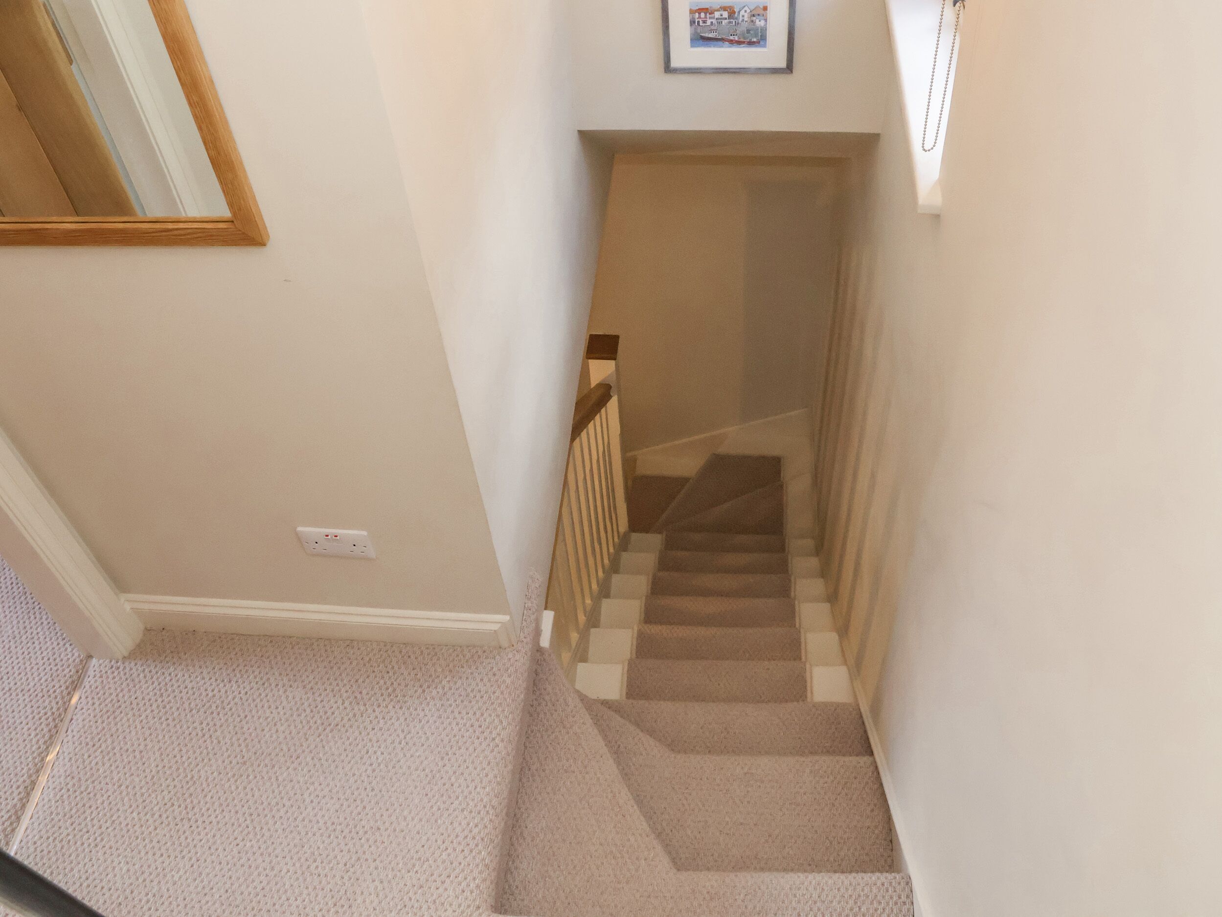 Un escalier recouvert de moquette, avec une rampe en bois, des murs blancs et un tableau encadré accroché au mur.
