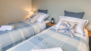 Duas camas de casal com roupa de cama azul e branca combinando, uma mesa de cabeceira com um candeeiro e um aplique de parede.