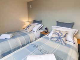 Duas camas de casal com roupa de cama azul e branca combinando, uma mesa de cabeceira com um candeeiro e um aplique de parede.
