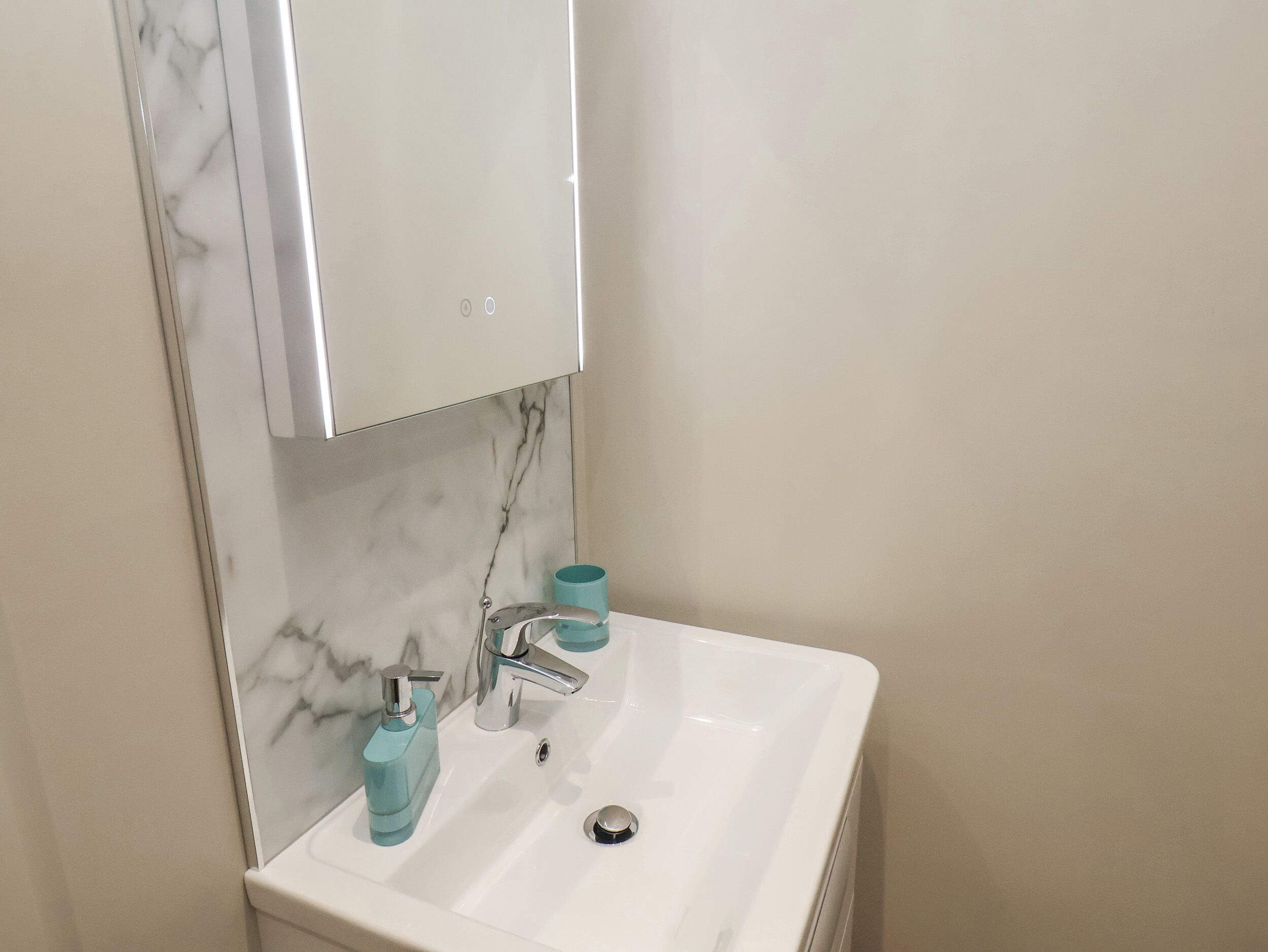 A bathroom with a white sink, a mirror, and a marble backsplash.
